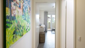 En hall som leder till ett badrum med en stor tavla på väggen, en korg av rotting och utsikt över omgivningen.