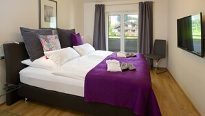 Ett modernt hotellrum med en stor säng, en tv och utsikt över ett hus genom fönstret.