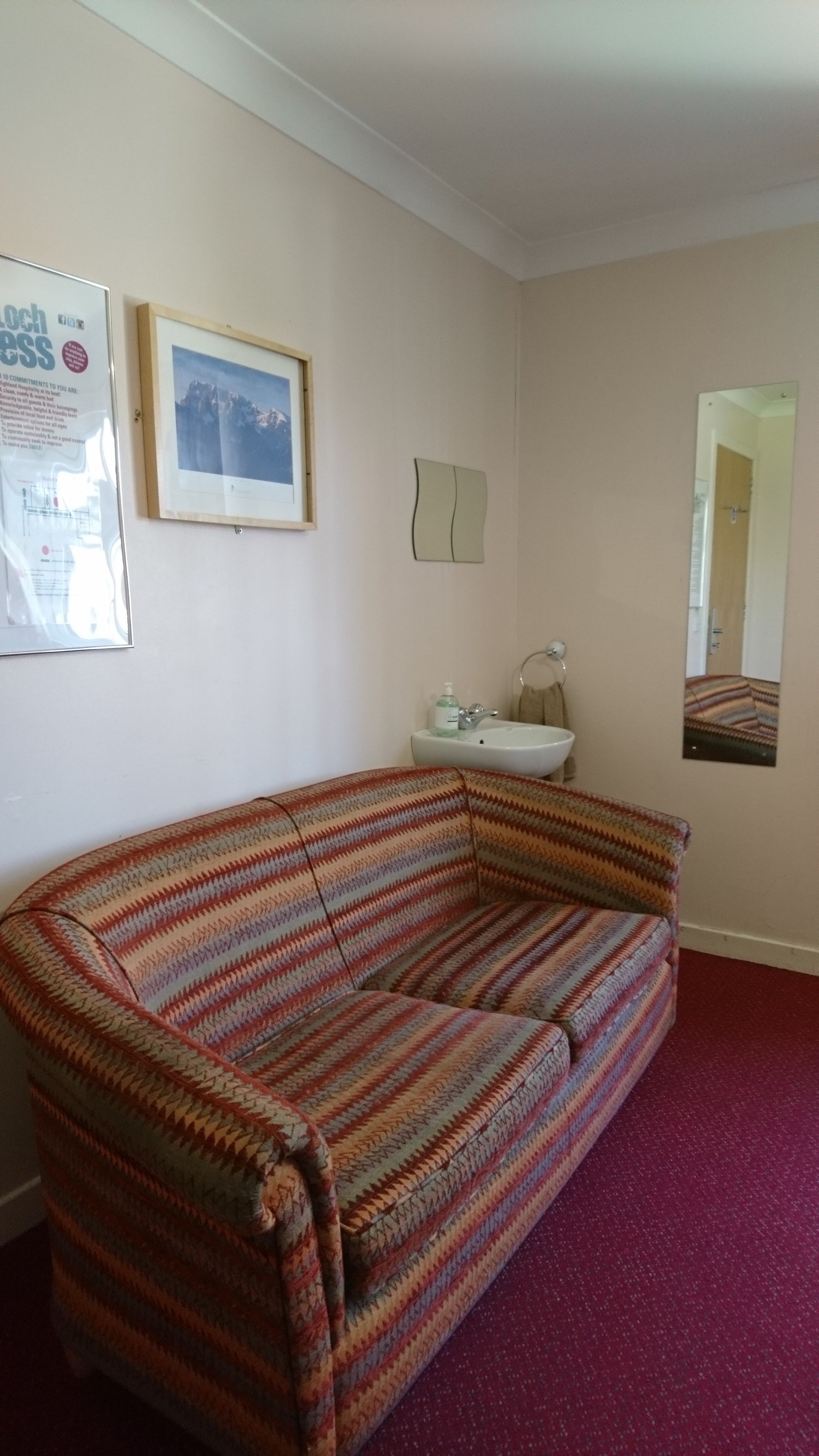 Ein Zimmer mit einem gestreiften Sofa, einem Waschbecken, einem Spiegel und einem gerahmten Bild an der Wand.