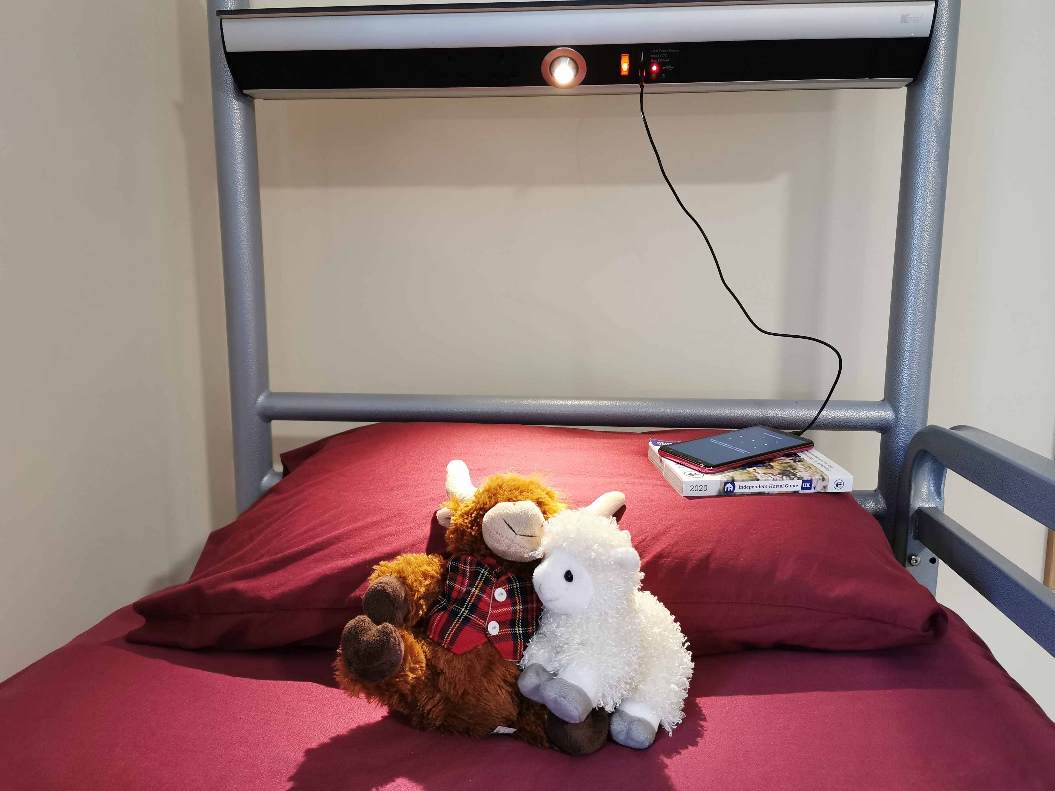 A bunk bed with a red mattress, a stuffed lamb, and a smartphone on the top bunk.