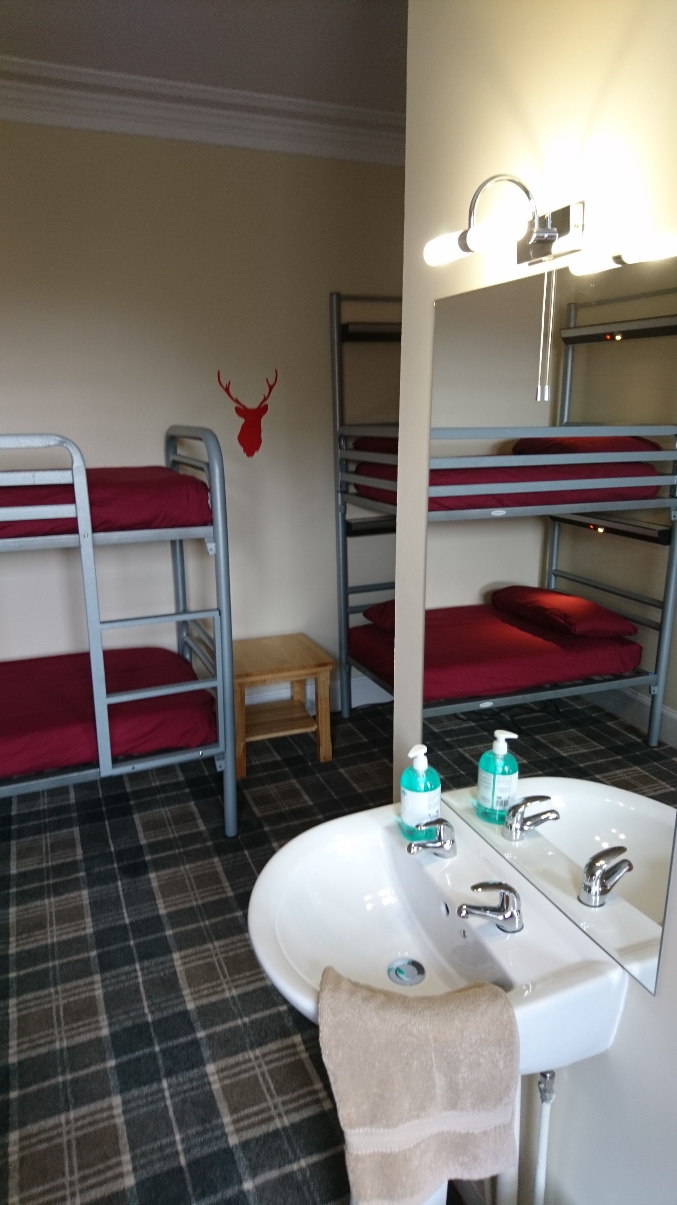 A bunk bed room with a small wooden stool, a sink with soap dispenser, and a mirror.