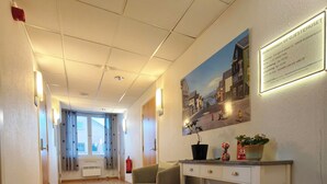 A hotel lobby with a wooden floor, a reception desk, a chair, a plant, and a painting on the wall. - Gjestehuset Kristiansund (Kristiansund)