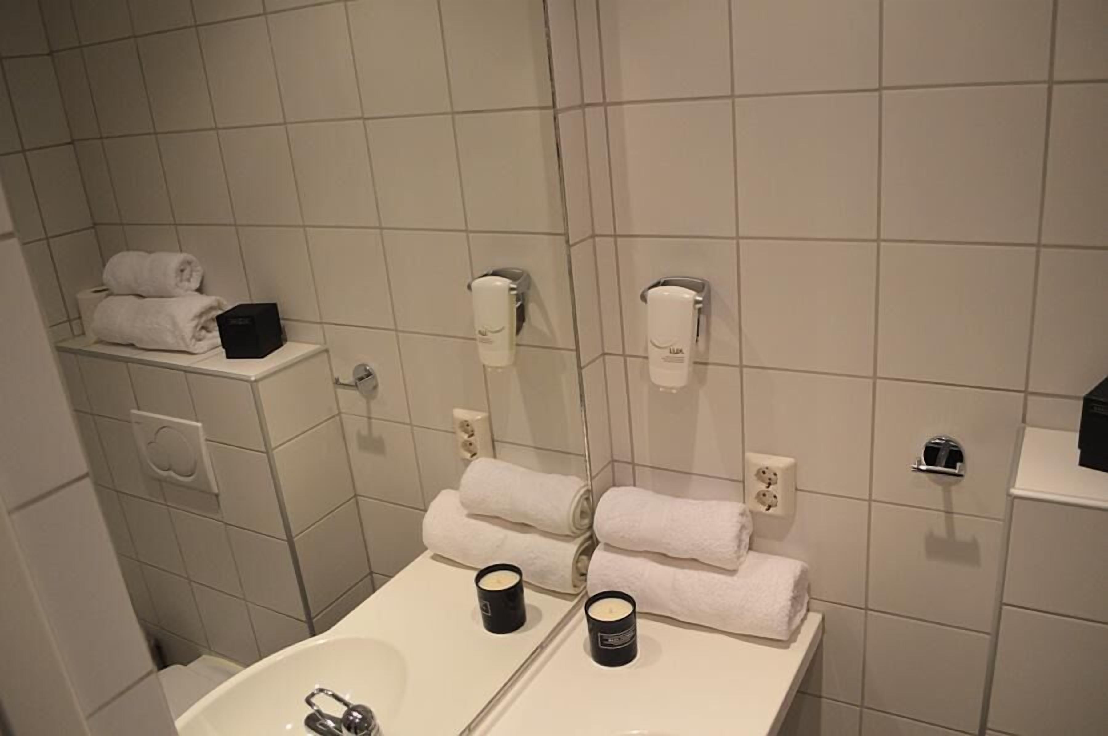 Ein Badezimmer mit Waschbecken, zwei Kerzen, einem Spiegel und Handtuchspendern.