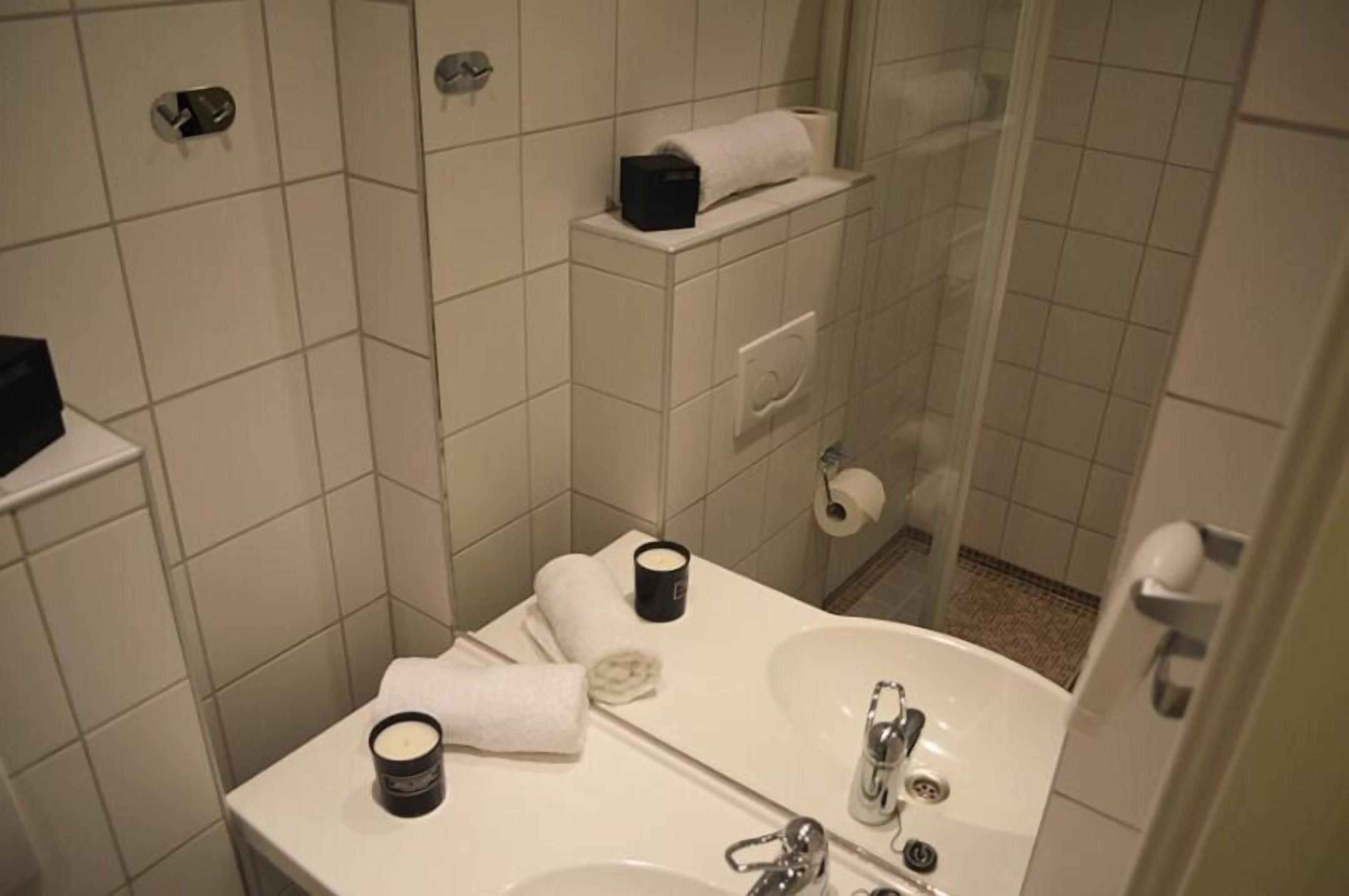 A bathroom with a sink, mirror, and shower. There are towels and toiletries on the counter.