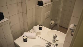 A bathroom with a sink, mirror, and shower. There are towels and toiletries on the counter.