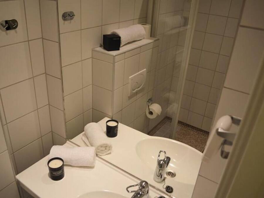 A bathroom with a sink, mirror, and shower. There are towels and toiletries on the counter.