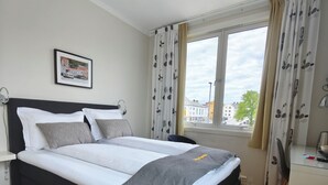 A modern hotel room with a bed, a desk, and a window with curtains. - Gjestehuset Kristiansund (Kristiansund)