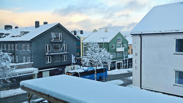 A snowy outdoor seating area with tables and chairs, a covered walkway, and buildings in the background. - Gjestehuset Kristiansund (Kristiansund)