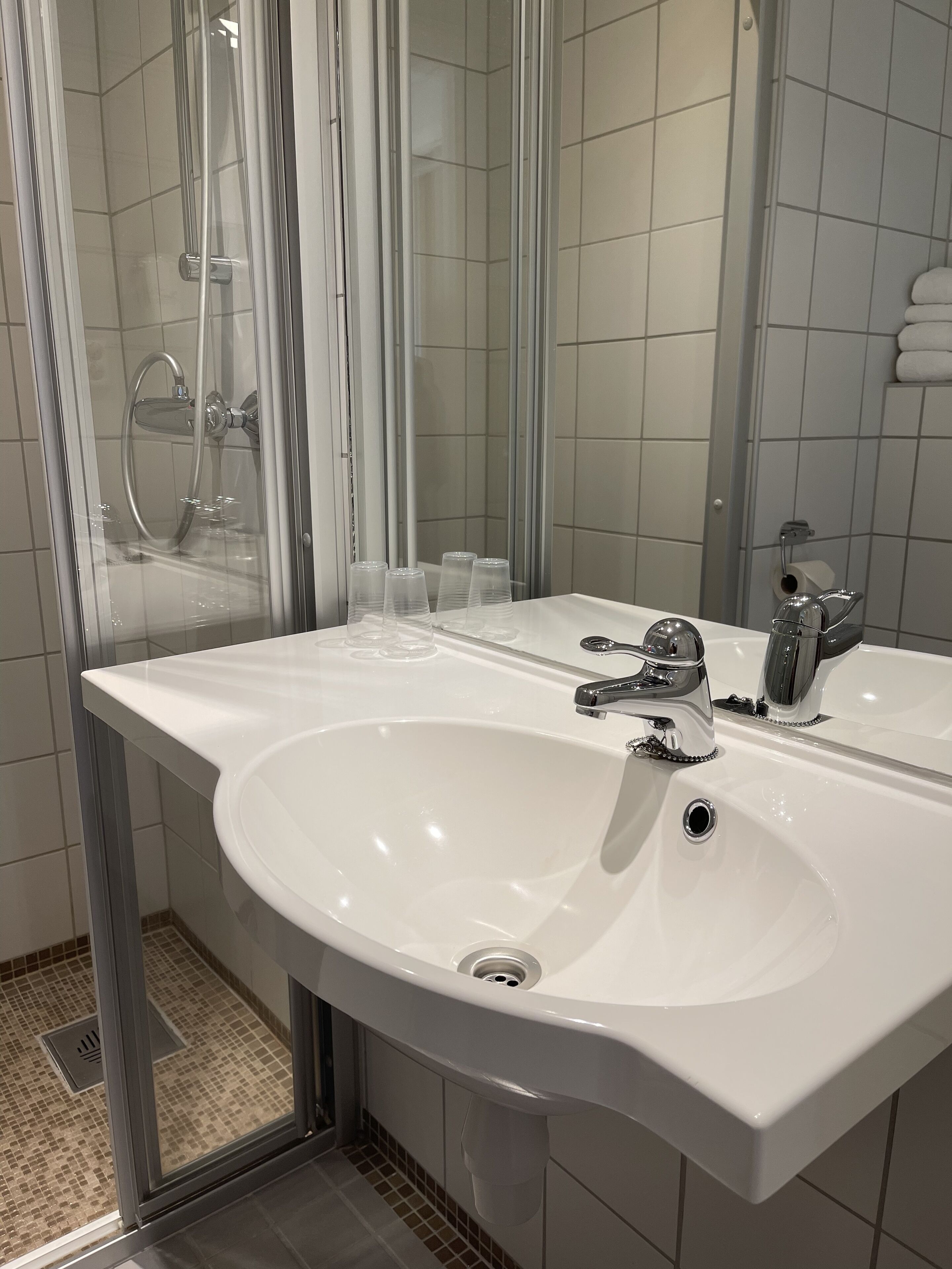 A bathroom with a white sink, a mirror, and a glass shower enclosure.