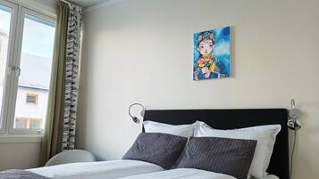 Uma cama bem arrumada com cabeceira preta, um quadro na parede e uma janela com cortinas.