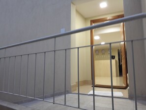 Eine Treppe mit Metallgeländer führt zu einem Empfangsbereich mit einer Holztür und einer an der Wand befestigten Uhr.