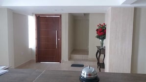 A hotel lobby with a wooden door, a reception desk, and a vase of red flowers. - Hotel Interlagos Xua (São Paulo)