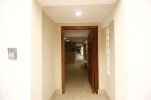 Ein Flur mit einer Holztür, die zu einem Zimmer führt. An der Wand befindet sich ein Lichtschalter und links ein kleines Gerät.