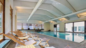 A large indoor swimming pool with multiple lounge chairs and a sunbed.