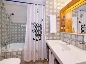 A bathroom with a patterned tile backsplash, a white sink, a mirror with a wooden frame, and a shower curtain with a cow design. - Schweizerhof Ferienwohnungen Lenzerheide (Vaz-Obervaz)