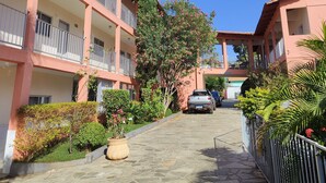Un edificio de varios pisos con balcones, un patio empedrado de piedra y un árbol alto.