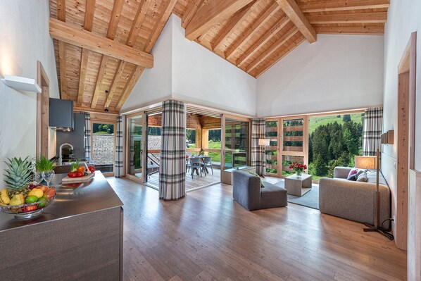 A spacious living area with wooden beams, large windows, and a view of a garden.