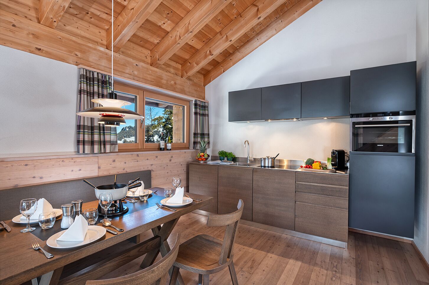 A modern kitchen with wooden beams, a dining area with a table set for two, and a view through the window.