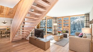 A modern living room with a wooden staircase, a sofa, a coffee table, and a TV. - Turrabuel (Churwalden)