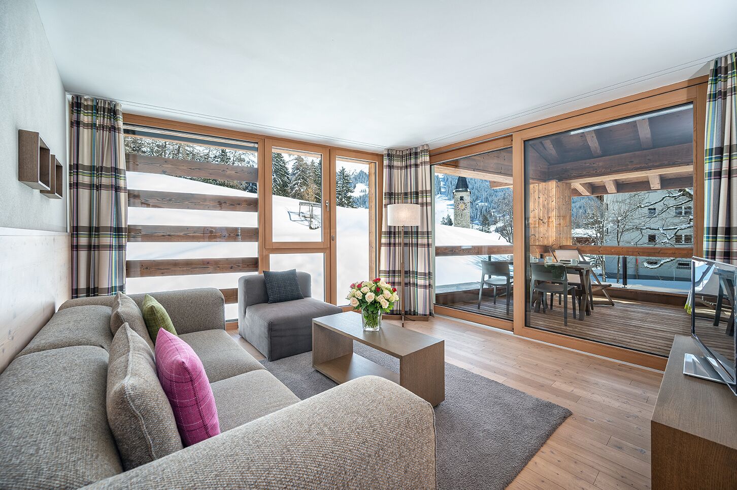 Ein modernes Wohnzimmer mit einer Couch, Sesseln, einem Couchtisch und Blick auf eine verschneite Landschaft durch große Fenster.