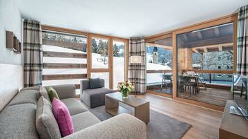 Ein modernes Wohnzimmer mit einer Couch, Sesseln, einem Couchtisch und Blick auf eine verschneite Landschaft durch große Fenster.