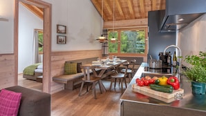 A modern kitchen with a wooden ceiling, a dining area with a bench, and a view of greenery outside. - Turrabuel (Churwalden)