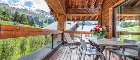 Une terrasse en bois avec une table et des chaises, offrant une vue sur un paysage montagneux.