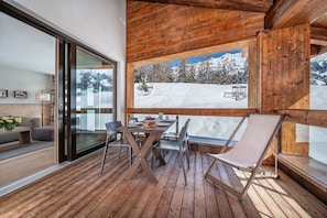 A wooden deck with a table and chairs, a sofa, and a large window overlooking a snowy mountain landscape. - Turrabuel (Churwalden)