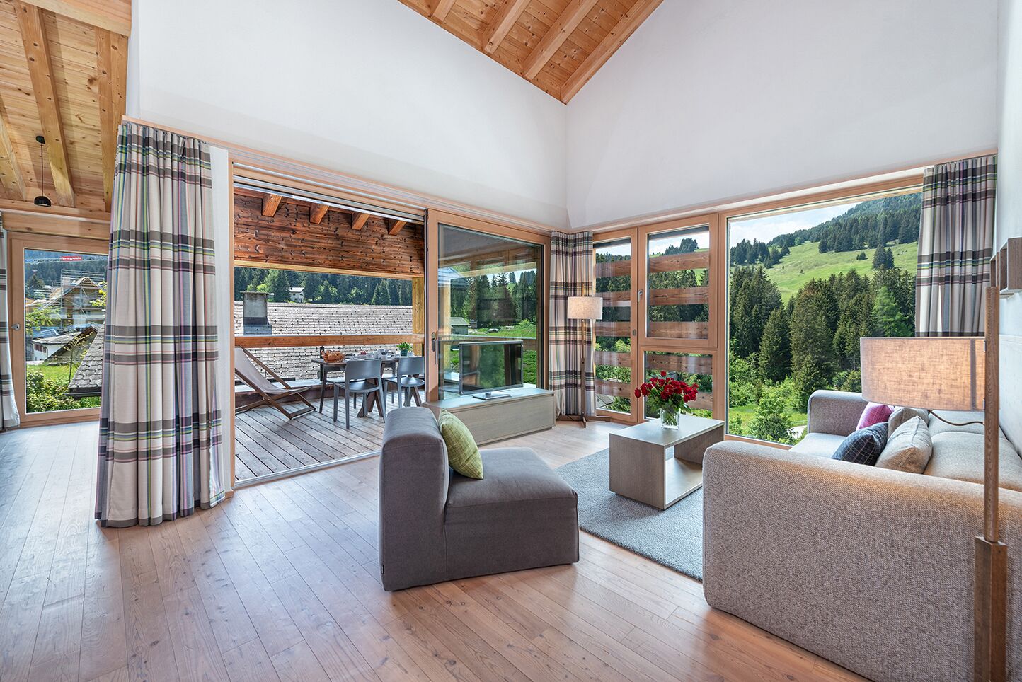 Ein großzügiger Wohnbereich mit Holzterrasse, großen Fenstern und Blick auf eine grüne Landschaft.