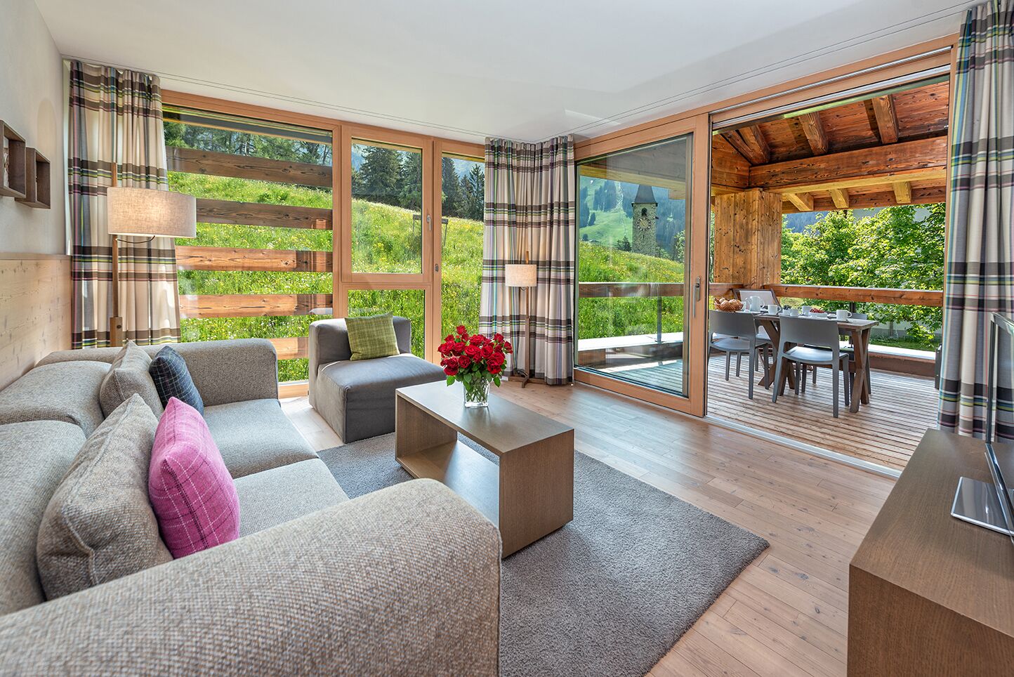 Ein modernes Wohnzimmer mit Sofa, Couchtisch und Blick auf eine Holzterrasse und Grünflächen.