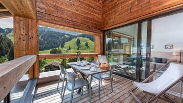 Une terrasse en bois avec une table dressée pour le repas, des chaises et un fauteuil de relaxation.