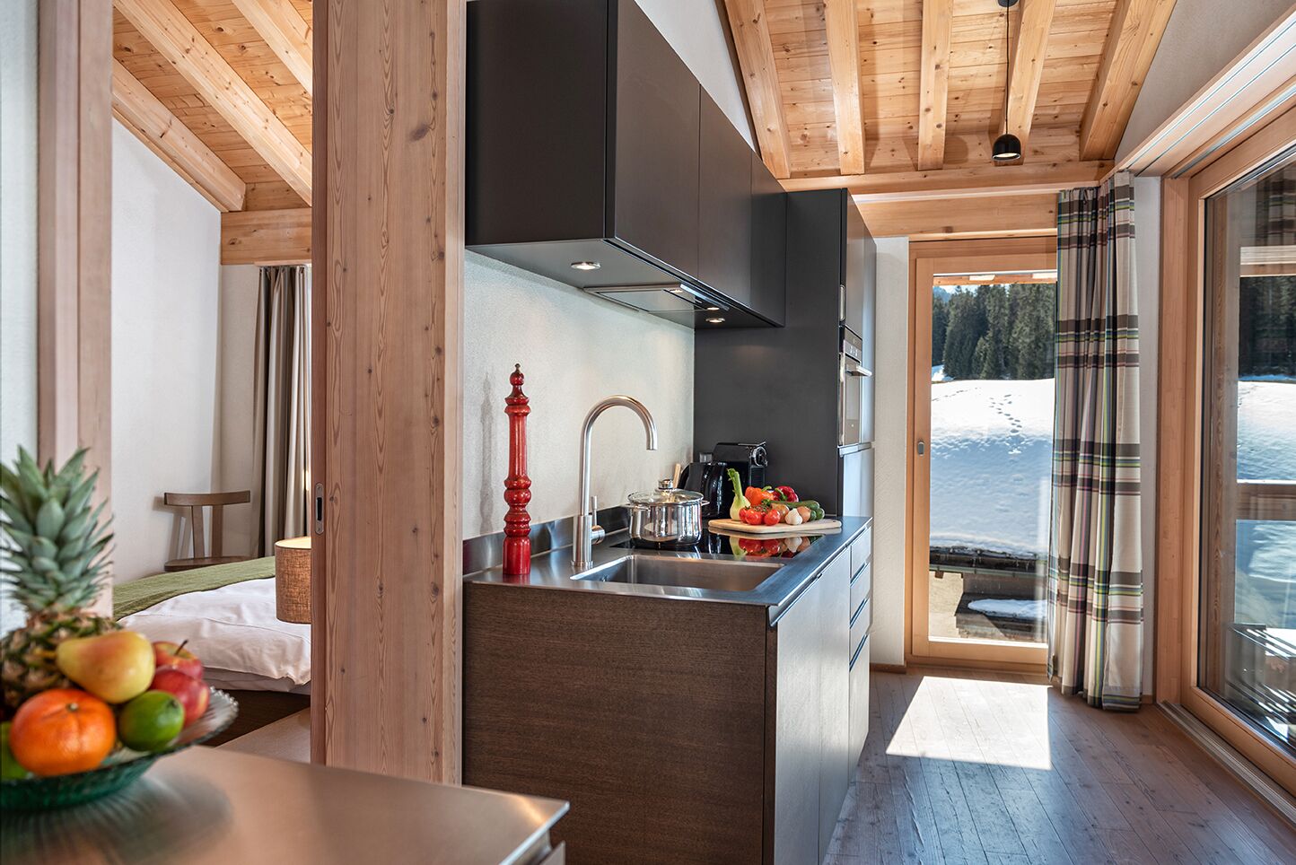 Une cuisine moderne avec un plafond en bois, un coin repas avec une table et des chaises, et une vue sur un paysage enneigé par de grandes fenêtres.