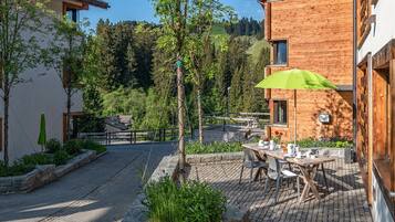 A courtyard with a wooden building, a table with chairs, and a green umbrella.
