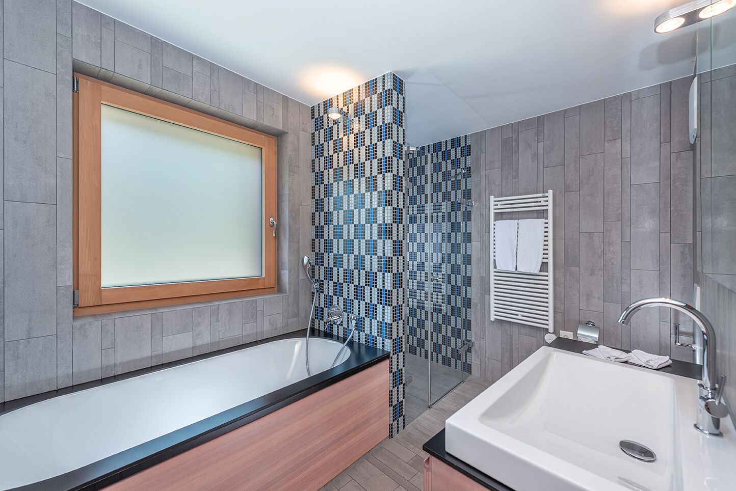 Ein modernes Badezimmer mit einer freistehenden Badewanne, einem Waschbecken inklusive Spiegel und einem Duschbereich mit Wand aus Mosaikfliesen.