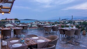 An outdoor dining area with tables and chairs, overlooking a cityscape and body of water. - Maison Vourla Hotel (Urla)