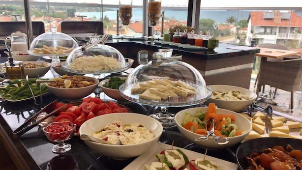 A buffet with various dishes, including salads, cheeses, and meats, set up on a table with a view of the sea. - Maison Vourla Hotel (Urla)