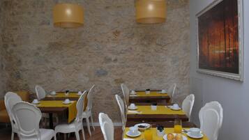 Comedor con paredes de piedra, sillas blancas, manteles amarillos y una pintura de atardecer.