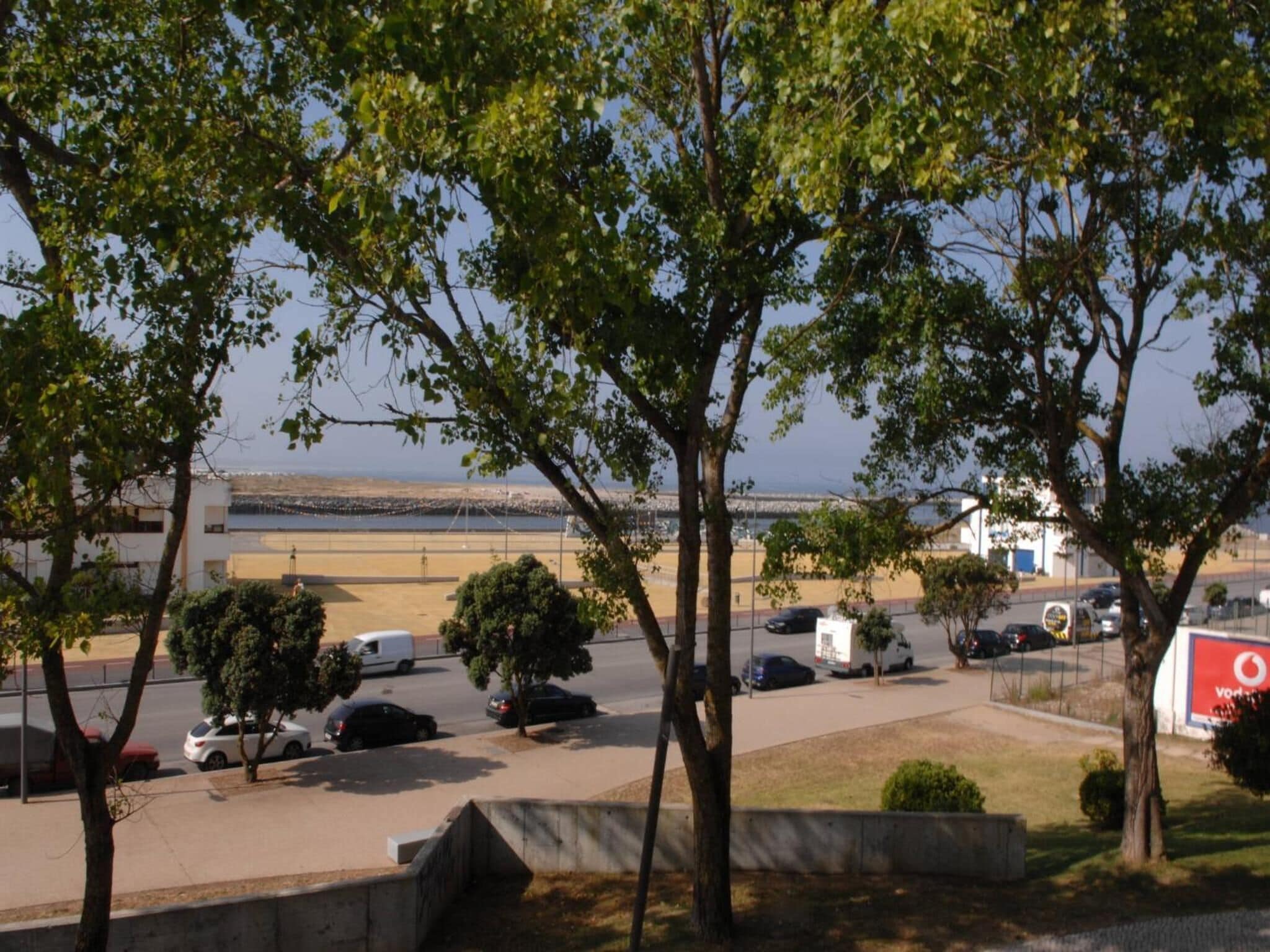 A parking area with trees and a view of a beach and a bridge.