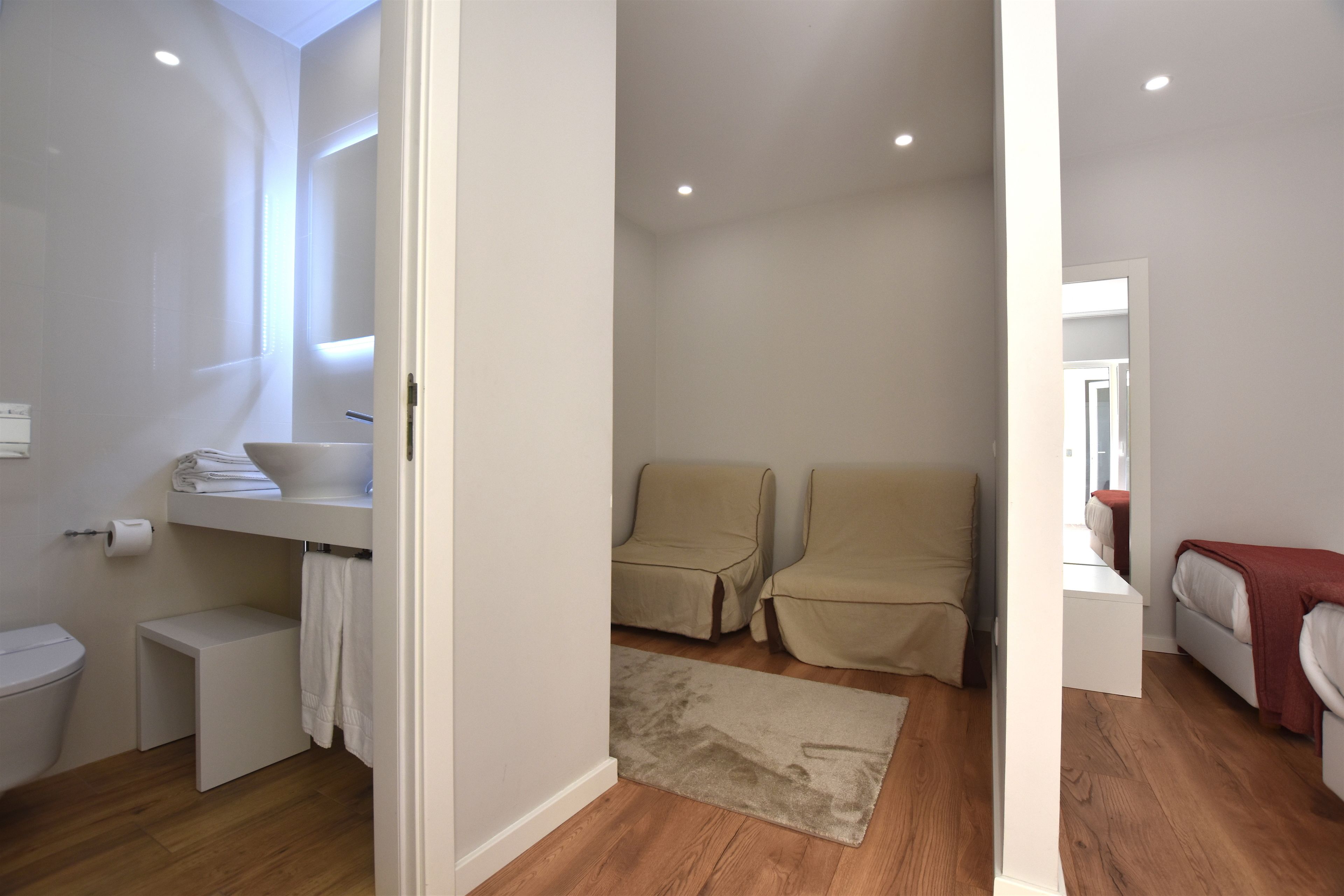 Een moderne badkamer met toilet, wastafel en handdoekhouder. Op de vloer ligt een klein bankje en een vloerkleed.