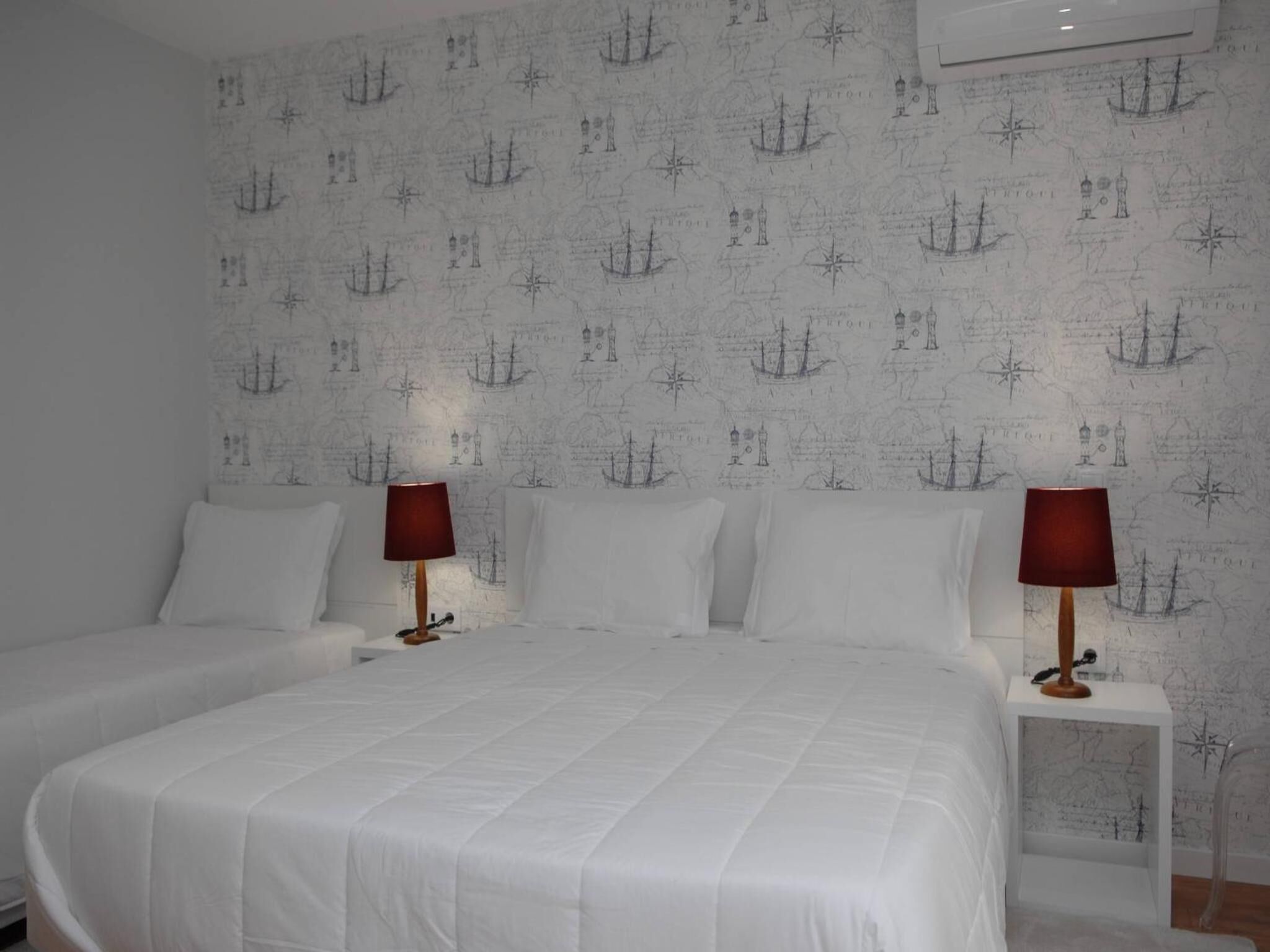 A hotel room with two beds, white bedding, and a wall with a nautical-themed wallpaper.