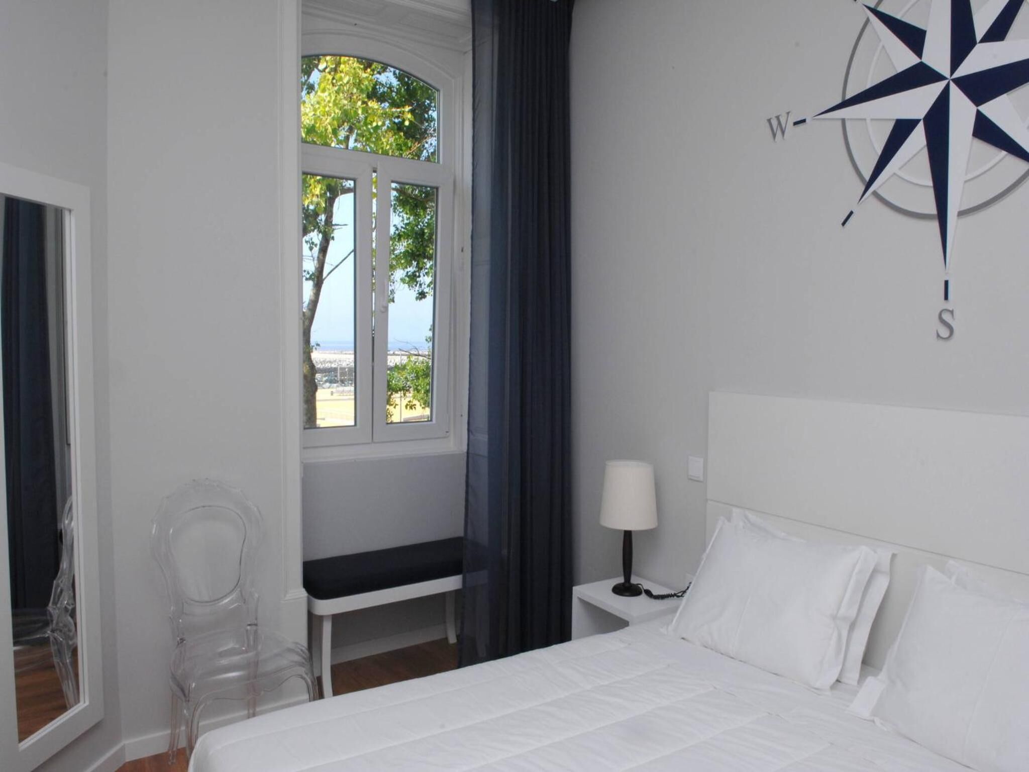 A hotel room with a large bed, a desk, a chair, a window with a view, and a compass wall decoration.