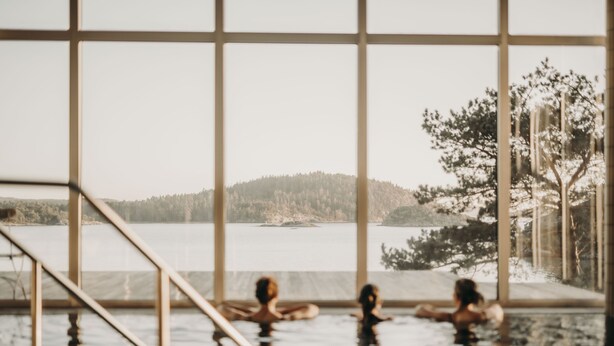 An indoor swimming pool with a view of a lake and forested hills. - Destination Bokenäset (Uddevalla)