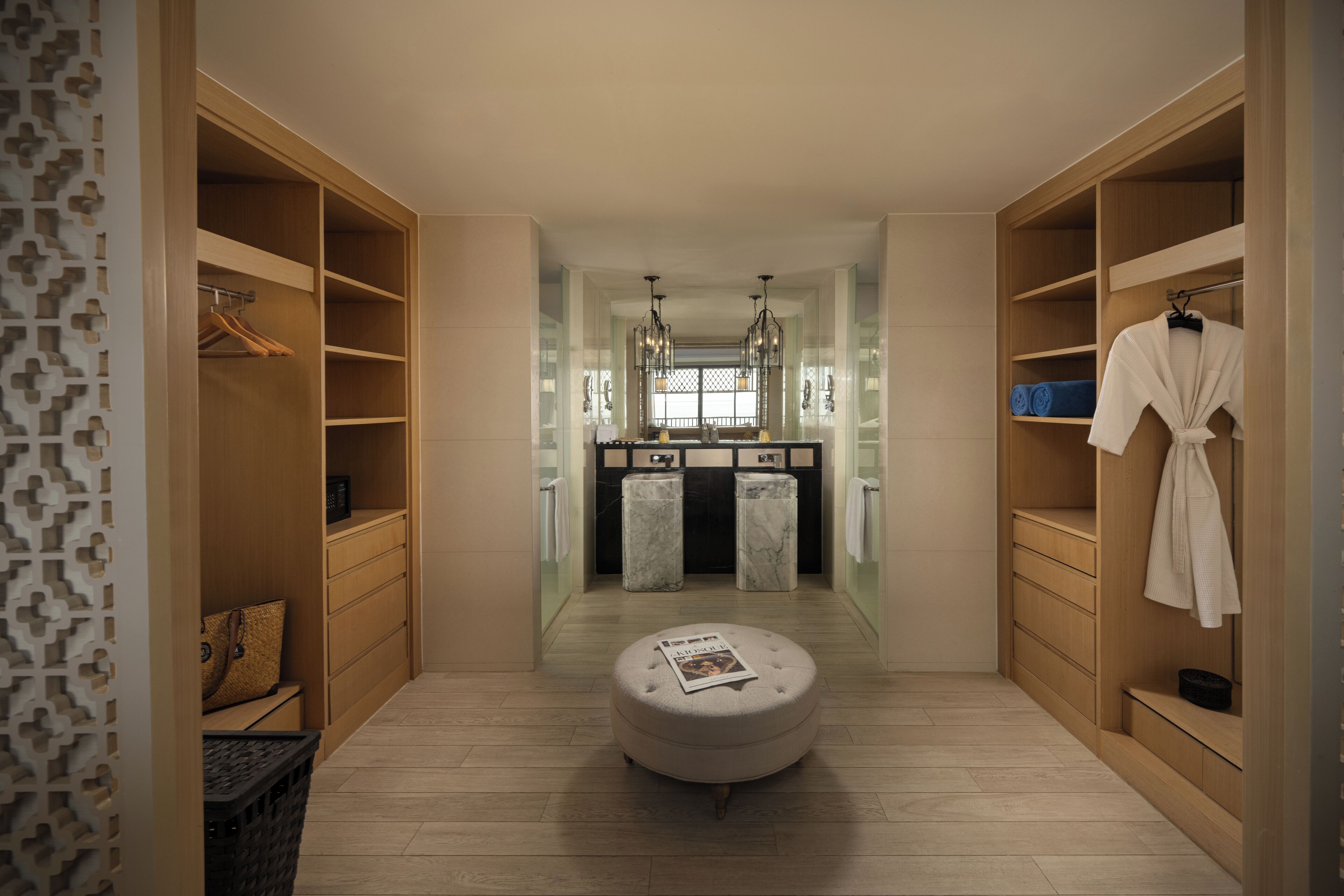 A walk-in closet with wooden shelving, a hanging robe, and a round ottoman with a magazine.