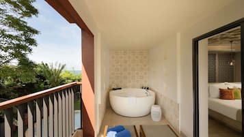 A balcony with a view of greenery, a large bathtub, and a white sofa with cushions.