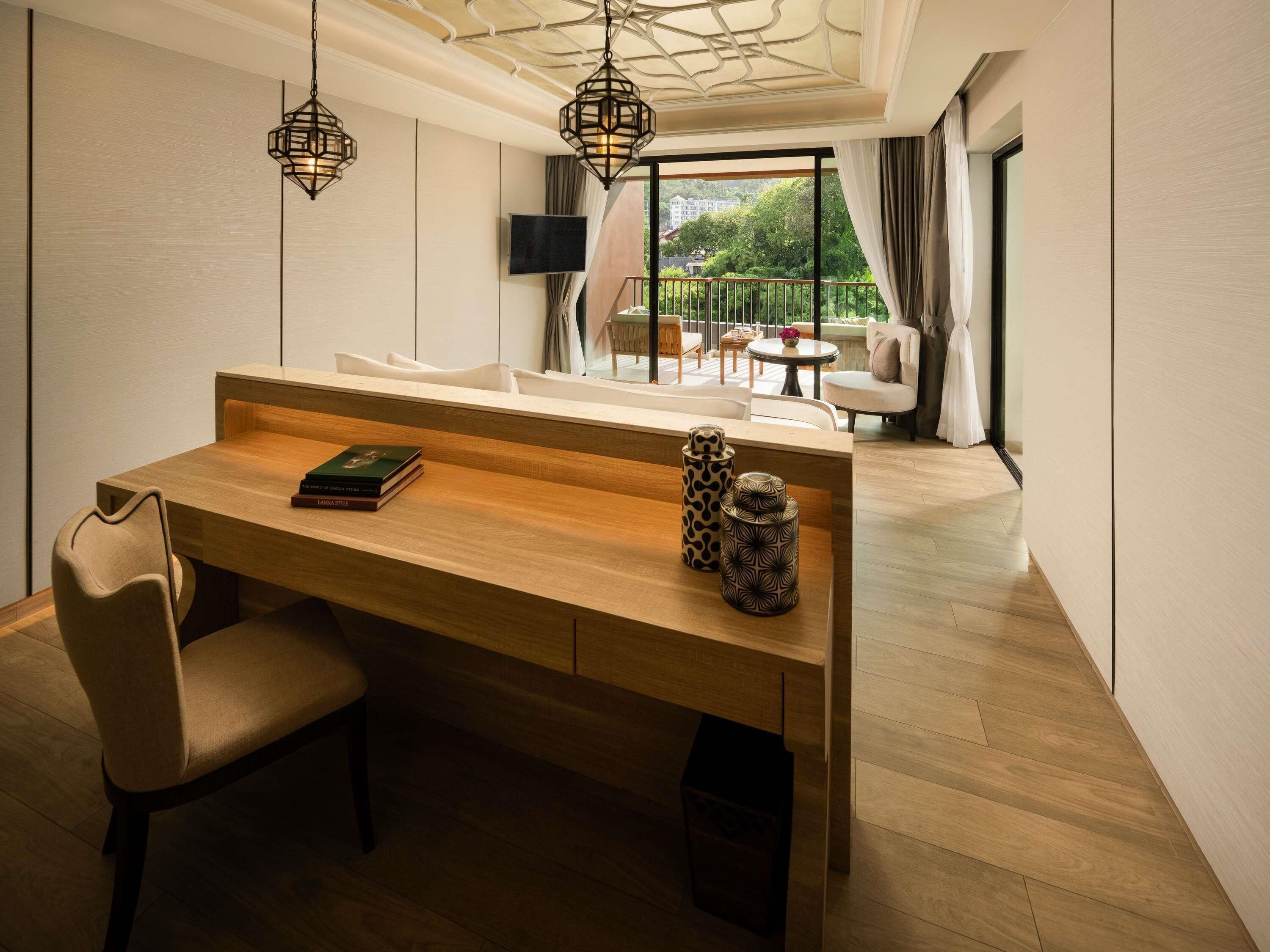 Una habitación de hotel moderna con un escritorio de madera, una silla, un televisor montado en la pared y un balcón con mobiliario exterior.