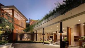 Une entrée d’hôtel moderne avec une allée couverte, des sièges extérieurs et une clôture décorative.