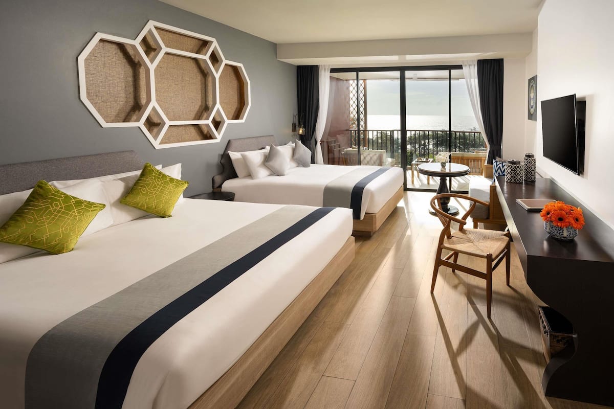 Een hotelkamer met twee bedden, een bureau, een stoel en een balkon met uitzicht.