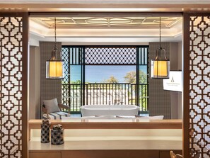 Une chambre d’hôtel dotée d’une grande baignoire, offrant une vue sur la mer, et séparée par une cloison en bois ornée d’un motif géométrique.
