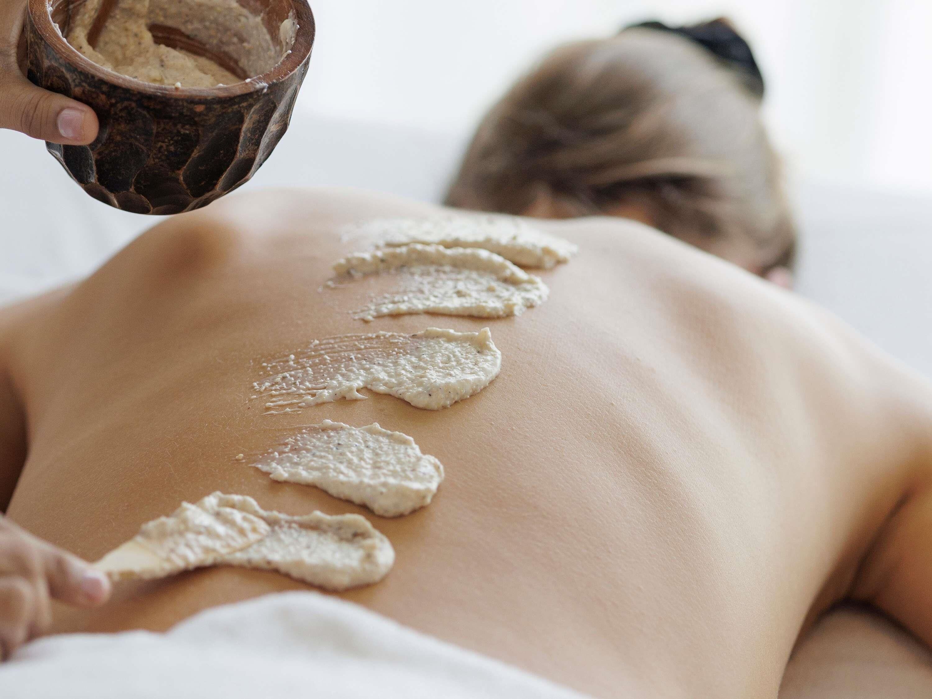 A person receiving a treatment with a brown container and a white substance applied to their back.