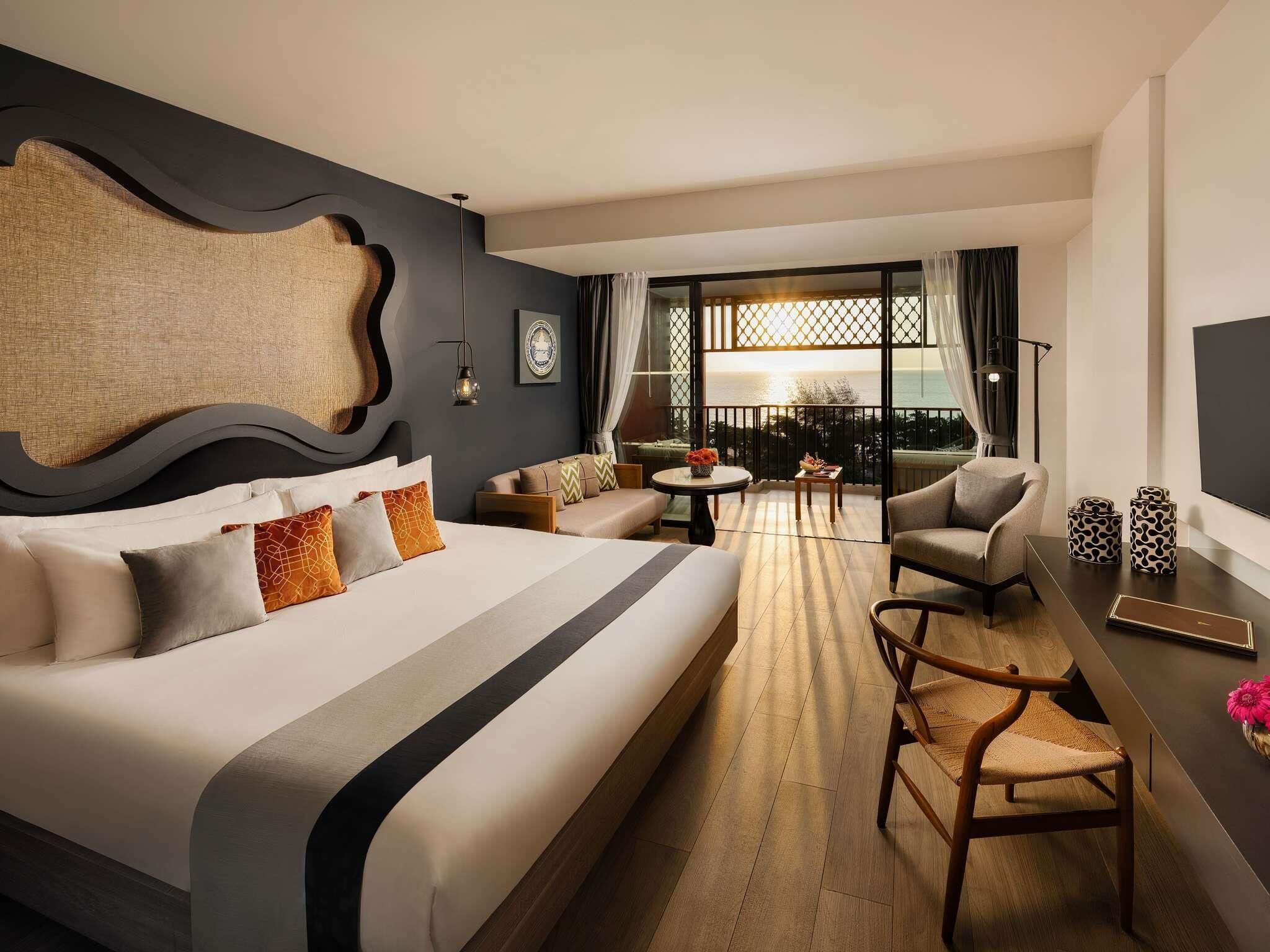 Una habitación de hotel moderna con una cama grande, un área de descanso con vistas y un balcón.